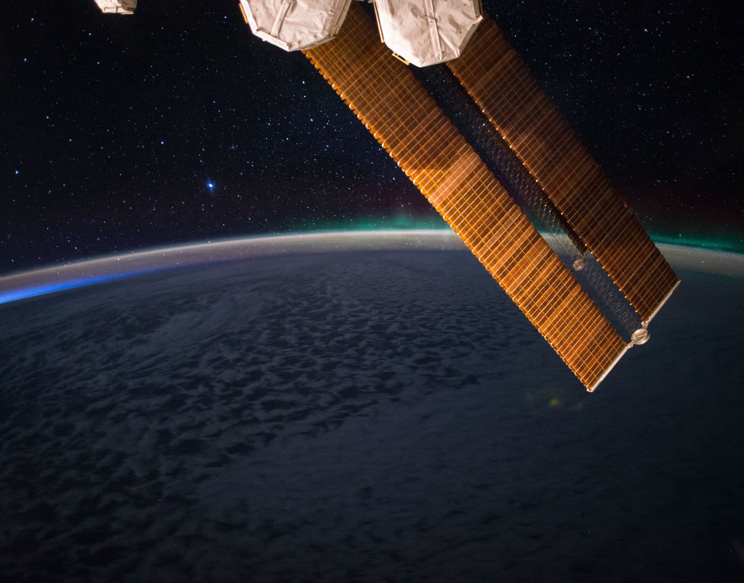 Copper-toned solar arrays of the International Space Station above a darkened night ocean
